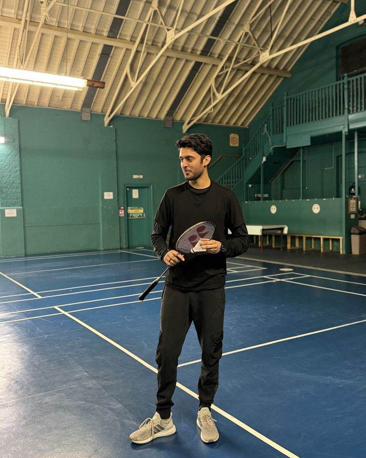 Muhammad holding a racket and shuttlecock on a badminton court at Enfield Drill Hall.